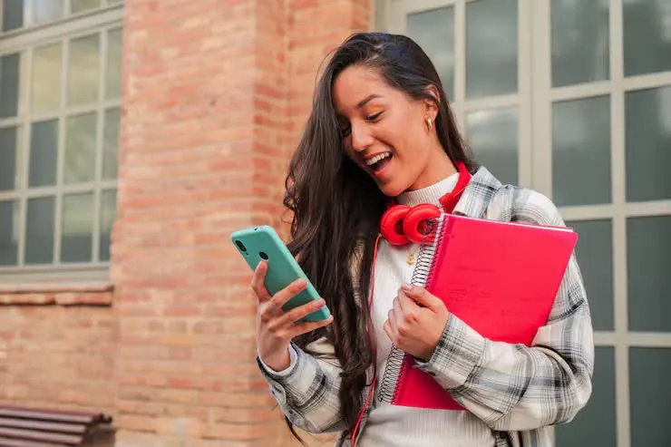 Estudante sorrindo no campus com celular e caderno